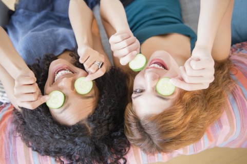 Women holding cucumber slices over eyes