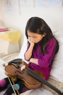 Pouting Vietnamese girl holding violin in bedroom