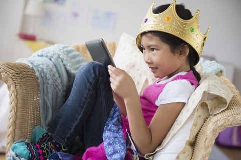 Vietnamese girl with crown using digital tablet in armchair