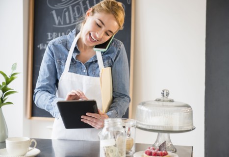 Caucasian barista using cell phone and digital tablet in cafe