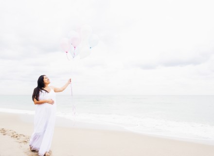 Pregnant mixed race woman holding balloons on beach