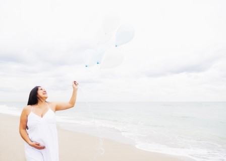Pregnant mixed race woman holding balloons on beach