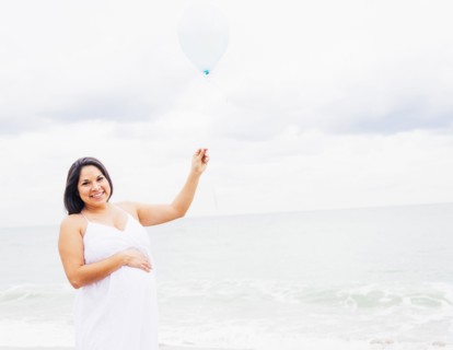 Pregnant mixed race woman holding balloon on beach