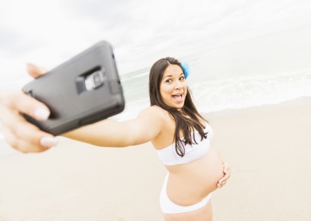 Pregnant mixed race woman taking cell phone photograph on beach