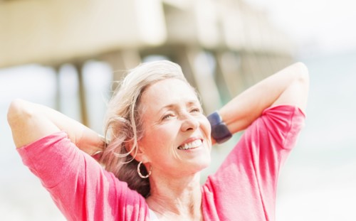 Older Caucasian woman with hands behind head on beach