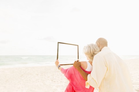 Older couple holding empty picture frame on beach