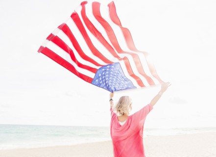 Older Caucasian woman holding American flag on beach