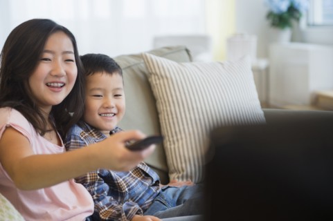 Asian brother and sister watching television on sofa