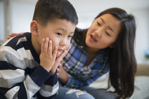 Asian sister comforting sad brother on sofa