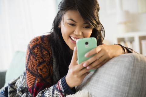 Pacific Islander texting with cell phone on sofa