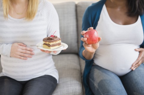 Pregnant women comparing apple and cake on sofa