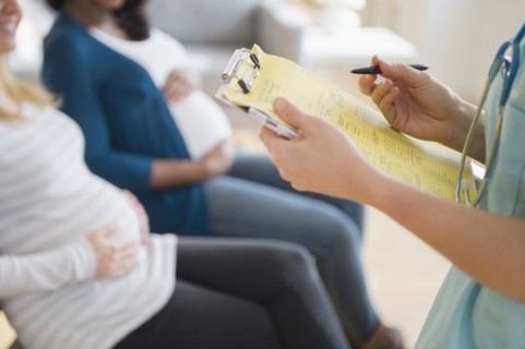 Nurse marking medical chart near pregnant women