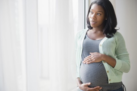 Black pregnant woman holding her stomach at window
