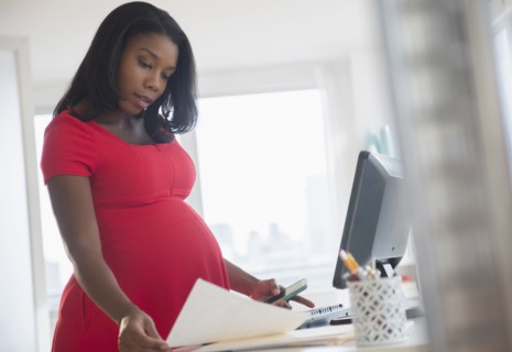 Black pregnant businesswoman reading paperwork at desk in office