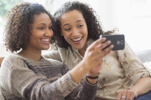 Smiling women taking cell phone photograph