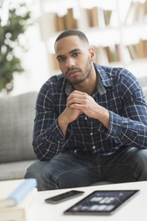 Hispanic man with cell phone and digital tablet in living room
