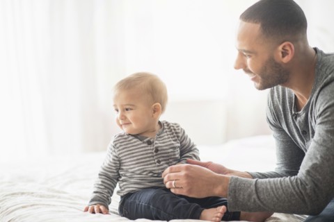 Father playing with baby son on bed
