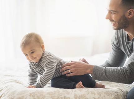 Father playing with baby son on bed