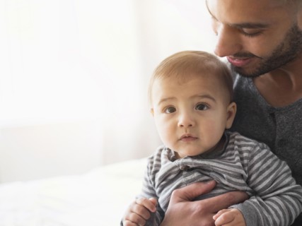 Smiling father holding baby son on bed