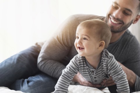 Smiling father playing with baby son on bed
