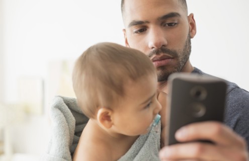 Father holding baby son and using cell phone