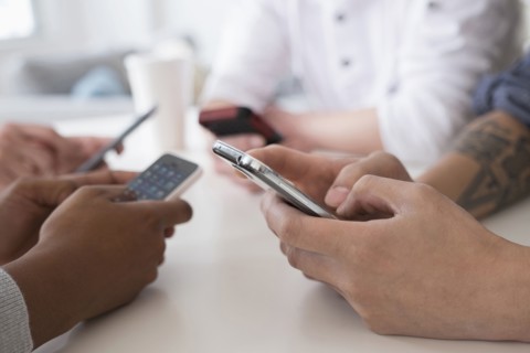 Close up of friends texting with cell phones at table