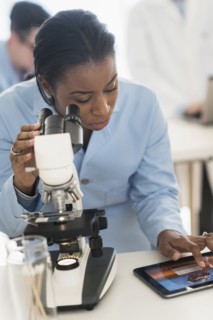 Scientist using microscope and digital tablet in research laboratory