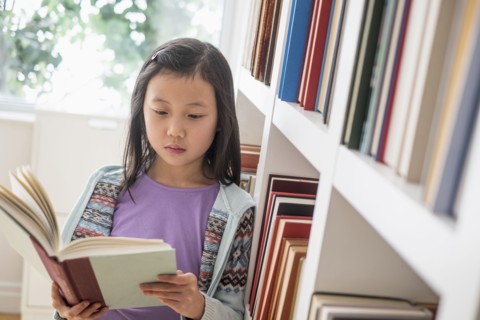 Chinese student reading book near library bookcase