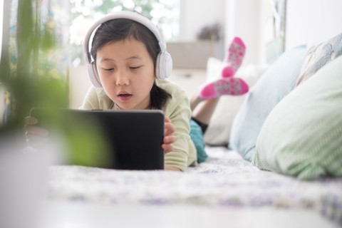 Chinese girl using digital tablet with headphones on bed