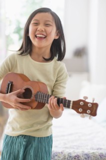 Chinese girl practicing ukulele in bedroom