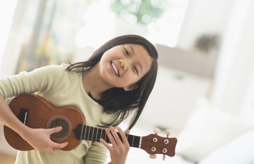 Chinese girl practicing ukulele in bedroom