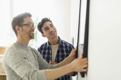 Caucasian gay couple hanging picture on wall