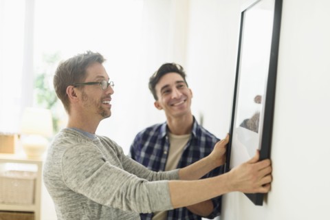 Caucasian gay couple hanging picture on wall