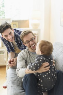 Caucasian gay fathers and baby relaxing on sofa