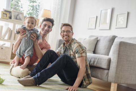 Caucasian gay fathers and baby playing in living room