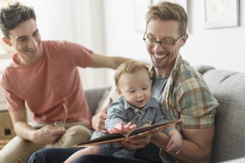 Caucasian gay fathers reading to baby in living room
