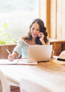 Chinese woman on cell phone using laptop in cafe