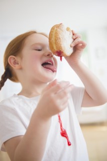 Caucasian girl licking messy jelly donut