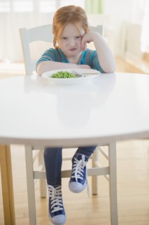 Caucasian girl pouting at plate of vegetables