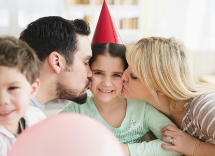 Caucasian parents kissing daughter at birthday party