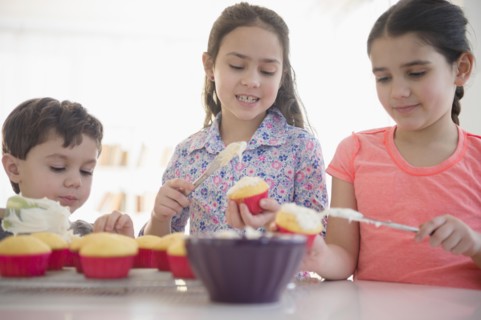 Caucasian siblings spreading frosting on cupcakes