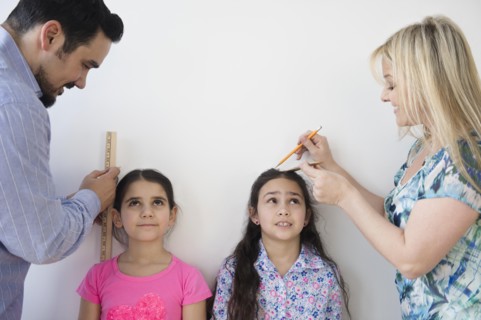 Caucasian parents measuring height of daughters on wall