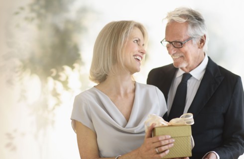 Smiling older Caucasian man giving wife a gift