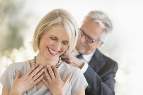 Smiling older Caucasian man giving wife a necklace