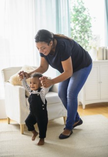Mixed race mother helping baby son walk in living room