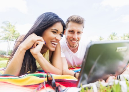 Hispanic couple using digital tablet on blanket in park