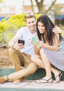 Hispanic couple using cell phones on sidewalk