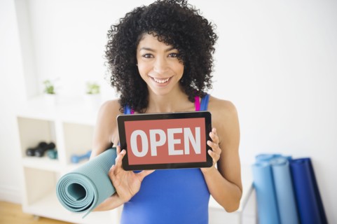 Mixed race woman holding open sign in yoga studio