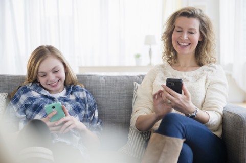 Caucasian mother and daughter using cell phones on sofa