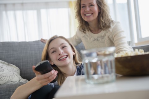 Caucasian mother and daughter watching television on sofa
